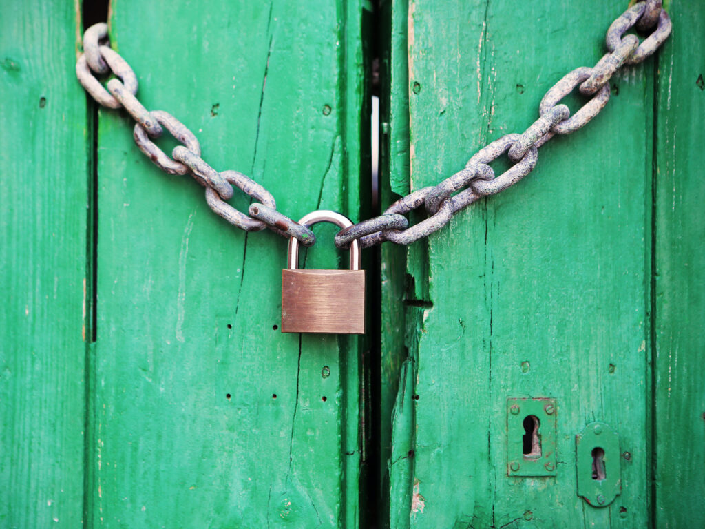 Brass padlock chained to a pair of green wooden doors depicting how Kids Online Safety Act could lead restrictions