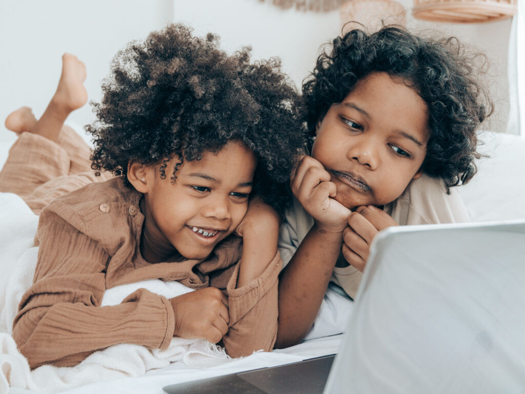 Two children with dark hair looking curiously at the internet on a silver laptop with black keyboard