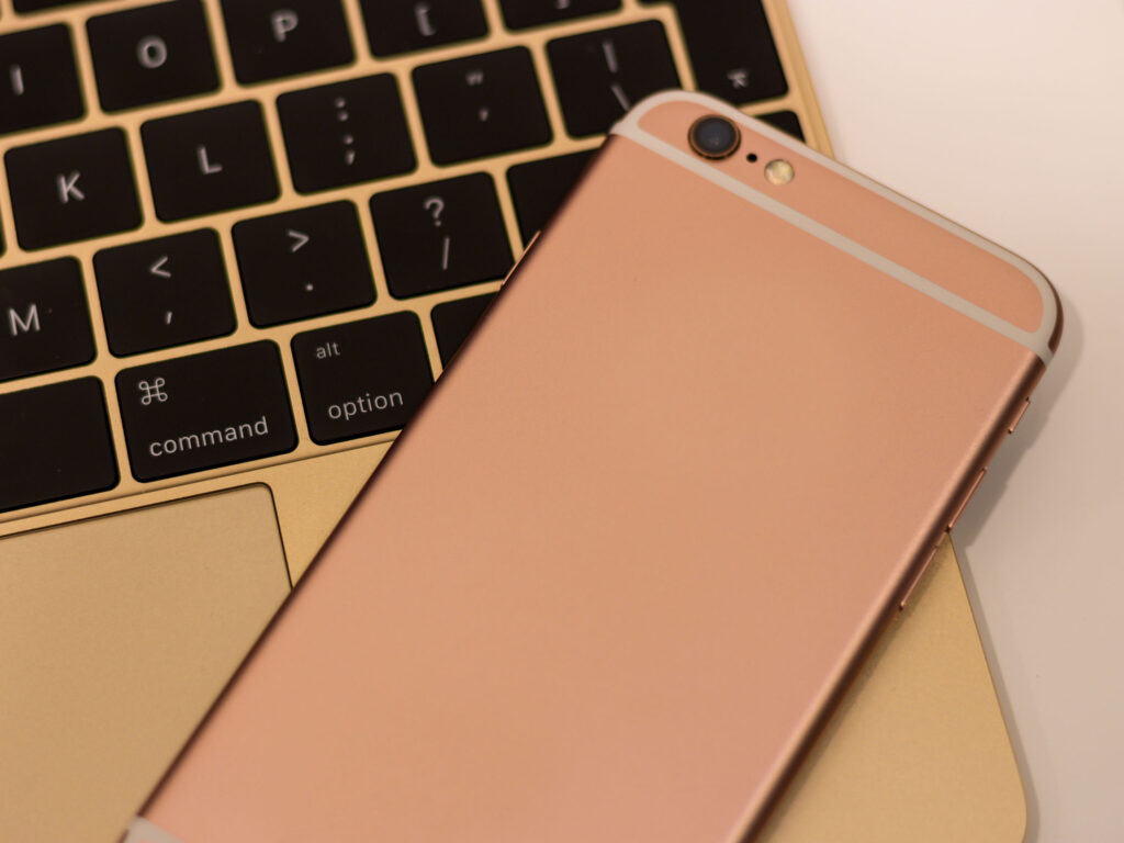 Rose gold mobile phone laying on top of gold laptop depicting how updated operating systems help to keep children safe online