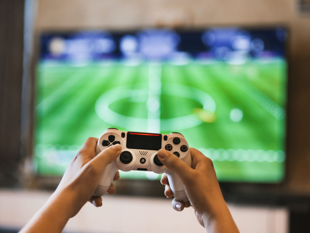 Child enjoying screen time with hands holding white game controller in front of TV