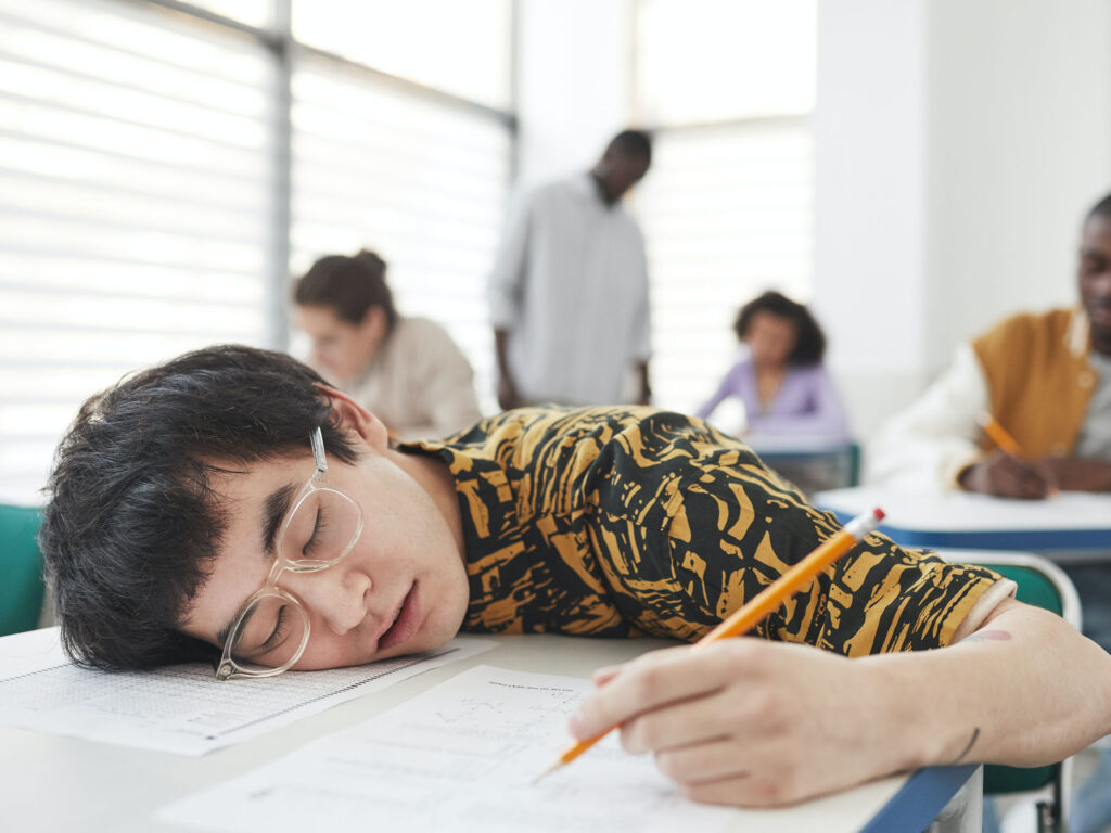 Older child falling asleep on a white examination desk whilst still clutching pencil due to excessive screen time